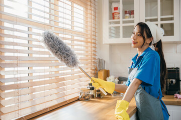 Smiling Asian woman holding duster cleans dirty window blinds. Ensuring purity and hygiene in...