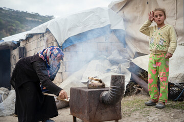 A refugee woman and her daughter cook with wood. The tragic humanitarian conditions of Syrian refugees. - obrazy, fototapety, plakaty