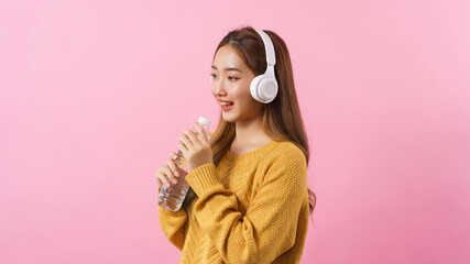 Young woman holding water bottle as microphone to singing a song isolated on pink background