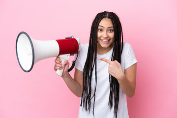 Teenager girl with braids over isolated pink background holding a megaphone and with surprise...