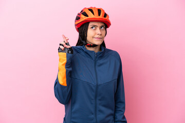 Teenager cyclist girl isolated on pink background with fingers crossing and wishing the best - obrazy, fototapety, plakaty