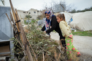 A refugee woman and her daughter cook with wood. The tragic humanitarian conditions of Syrian...