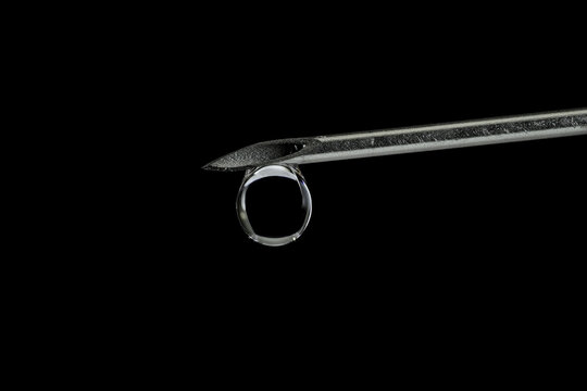 A syringe's needle barrel tip with a water droplet hanging from. - Powered by Adobe