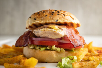 Grilled chicken breast sandwich with bacon, lettuce, onion rings and cheese served with a side of fries.