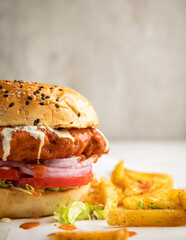 Fried chicken breast sandwich with mayonnaise, lettuce, ringed onion, pickle and tomato served with a portion of French fries