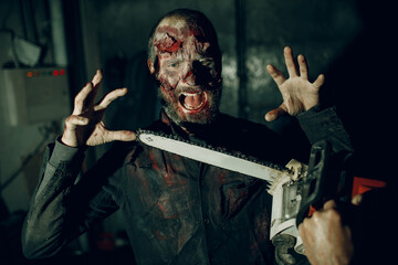 Walking zombie dead man and chainsaw attack on horror halloween party.