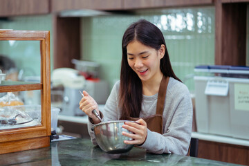 Asian young female chef cooking egg in bowl for bakery. small business owner and Bakery Concept.