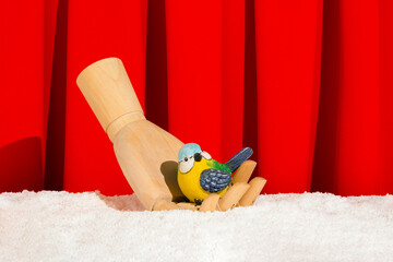 Creative scene a colorful bird on wooden fist on the snow. Minimal idea with ceramic songbird and...