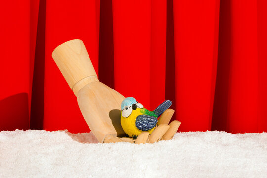 Creative scene a colorful bird on wooden fist on the snow. Minimal idea with ceramic songbird and red curtain.