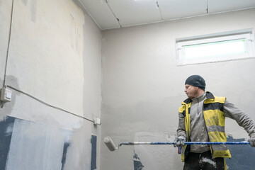 Skilled Worker in Work Attire Paints Interior with Precision Using Roller.