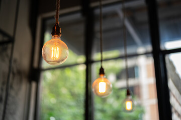 A classic style lightbulb is glowing in orange warn lighting is hanging down from ceiling with...