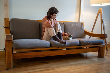 Sad depressed woman sitting on sofa, stroking adorable breed cat Devon Rex. Lonely teen girl in...