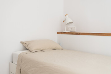Single bed near wall shelf with night lamp in white bedroom