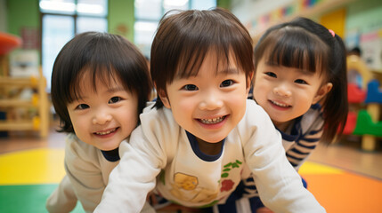 日本の幼稚園児・保育園児3人が長袖の私服でカメラに向かってきて笑っている写真、背景教室、保育室 - obrazy, fototapety, plakaty
