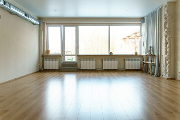 Fototapeta premium A spacious empty hall with columns and large windows. A gym with wooden floors for yoga and fitness classes. Interior design of the fitness center. A large room without furniture.