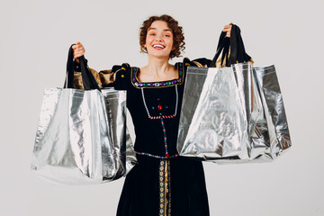 Young adult smiling woman dressed in a medieval dress holding shopping bags in hands isolated white...