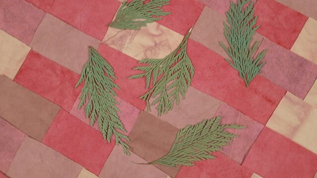 Dried thuja twigs lie on a handmade background in patchwork style with cotton fabric elements in red tones