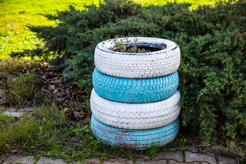 Stack of old used car tires painted white and blue on the grass in the garden.