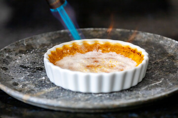 Crème brûlée, creme brule. Classic creme brulé being flambé. Burning, flaming, ramekins, vanilla beans, blowtorch, sugar