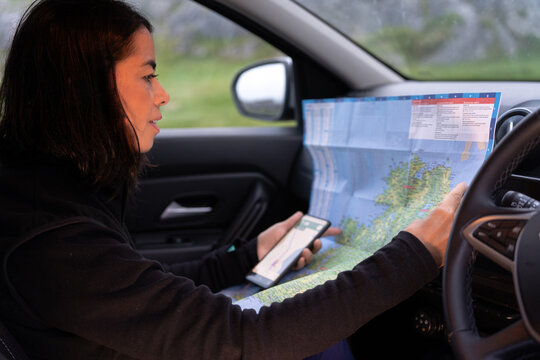 Woman checking the map and her cell phone inside her vehicle to decide what to do next on her car trip