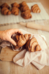 Unrecognizable person takes two golden brown color, with flaky, buttery crust croissants from natural cotton fabric wooden table. Concept of food, bakery, cuisine, desserts, cooking.