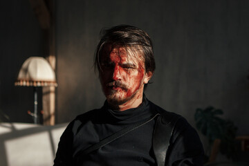 a tired man with a broken face covered in blood sits by the window. guy with makeup, cosplay