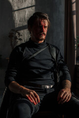 Fototapeta na wymiar a tired man with a broken face covered in blood sits by the window. guy with makeup, cosplay