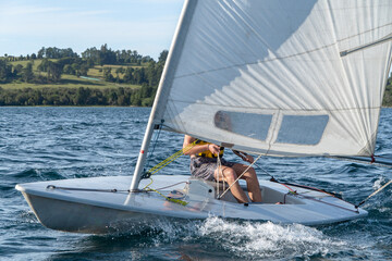 View of a small sailboat sailing on a windy summer day on the lake.