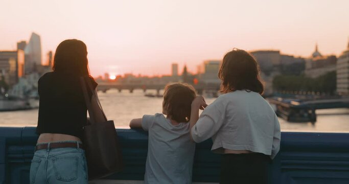 Cinematic shot of young mother talking with teenage children and admiring sunset view together. Tower Bridge, London