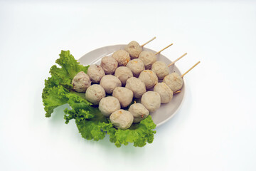 Tasty roasted pork meatballs skewers and lettuce on dish with white background. Meatballs Made from meat. Asian Street Food. Delicious grilled pork meatballs on skewers with vegetable in white plate.