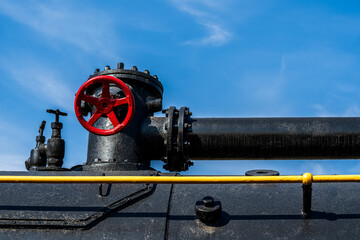 Rusty valve in a steam locomotive, red valve tap on a sky background.