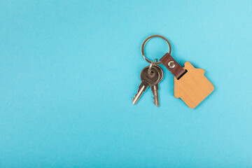 Keychain in the shape of a house with a key ring on a blue background. Concepts for real estate and moving home or renting property. Buying a property. Mock-up keychain house shaped.Copy space.