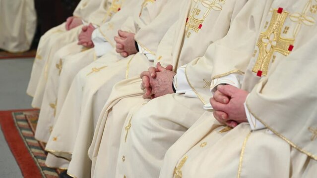 Catholic priests in liturgical vestments praying with hands folded. Hands of Christian man praying in Cathedral. Christmas Midnight Mass in church.	