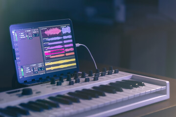 Musical keyboard and tablet in a dark room, music production.