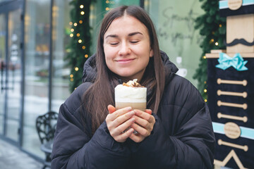 A young woman drinks coffee with cinnamon and anise in a cafe outside.