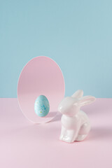 Creative concept with Easter bunny and egg in mirror on pastel pink table. Minimal Easter holiday idea.