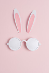 Creative Easter concept with bunny ears and white sunglasses on pink background. Minimal Easter concept.