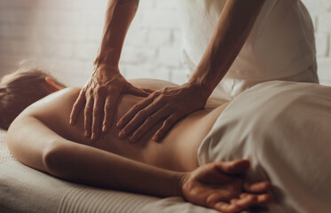 Hands of female chiropractor massaging back of young woman lying on massage table on white...