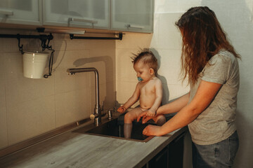Obraz premium baby bathes in the kitchen sink. Mom watches the child.