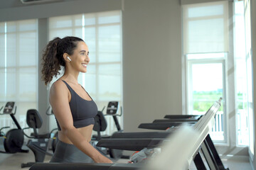 Fototapeta premium Happy healthy hispanic woman practicing a cardio exercise by running and walking on treadmill machine in fitness and using fitness tracker or smartwatch to track workout progress.