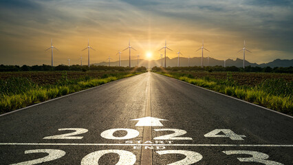 Word 2024 written on the road in the middle of asphalt road to wind generators at sunset.Concept of...