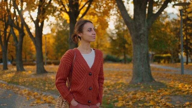 joyful smiling woman wearing knitted sweater or cardigan walks in maple park with golden foliage. Woman in nature at warm fall day. Active lifestyle. Female outdoors. girl walk in autumn park