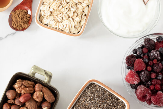 Healthy Organic Fiber Food Ingredients For Breakfast Preparation. Frozen Fruit, Nuts, Chia Seeds, Cinnamon, And Greek Yogurt On White. Top View.