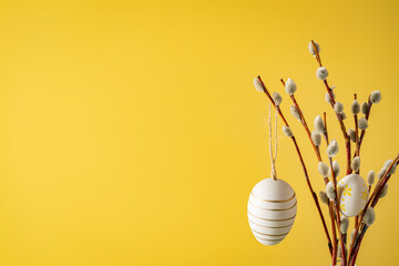 Spring Easter holiday yellow background with easter decor. Willow branches in a glass vase and easter eggs