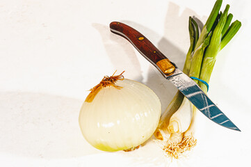   top view, medium distance of, a half a yellow onion, four scallions and knife with serrated blade, on white counter