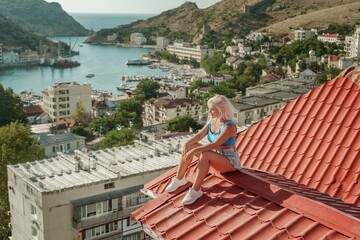 Woman sits on rooftop, enjoys town view and sea mountains. Peaceful rooftop relaxation. Below her,...