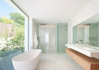 Spacious modern bathroom with marble walls, a freestanding bathtub, and a view of the garden through large windows