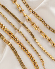 Set of gold chain bracelets on cream silk fabric - obrazy, fototapety, plakaty