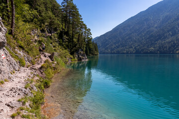 Panoramic hiking trail along east bank of alpine lake Weissensee, Carinthia, Austria. Glistening turquoise water mirrors the beauty of untouched nature. Scenic view of tranquil forest in summer