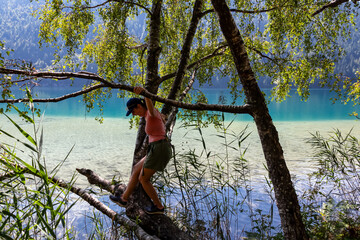 Fototapeta na wymiar Woman standing on tree branch with scenic view of alpine landscape at east bank of lake Weissensee, Carinthia, Austria. Serene landscape. Remote untouched nature in summer. Pristine turquoise water